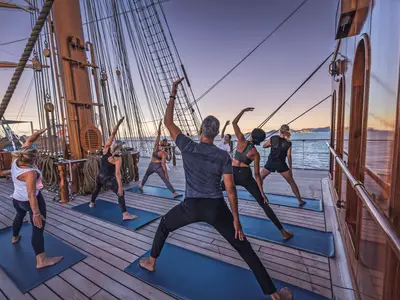 Eine Gruppe von Gästen macht Yoga-Übungen auf Yoga-Matten auf dem Holzdeck der Sea Cloud Spirit auf hoher See.