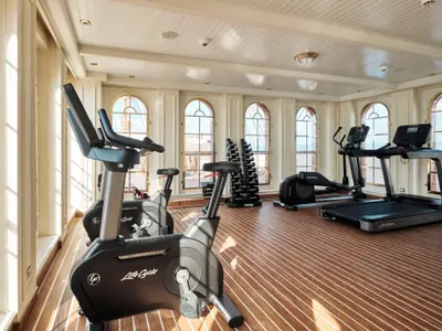 Heller Fitnessraum an Bord der Sea Cloud Spirit mit Trimmrädern, Laufband und Hanteln vor Bogenfenstern.