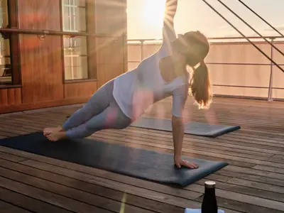 Eine Frau macht im warmen Sonnenlicht der Abendsonne Yoga auf einer Matte an Deck der Sea Cloud Spirit.
