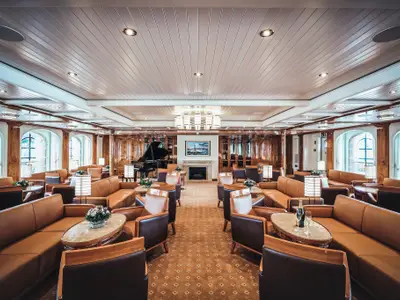 Elegante Lounge an Bord der Sea Cloud Spirit mit braunen Ledersesseln, Holztischen und einem Flügel.