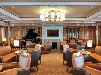 Elegante Lounge an Bord der Sea Cloud Spirit mit Ledersesseln, Flügel-Klavier, Holzwänden und Kronleuchter.