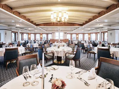 Blick in das stilvolle Restaurant an Bord der Sea Cloud Spirit mit weiß gedeckten Tischen und edler Holzdecke.