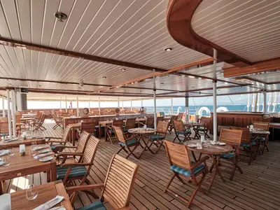 Überdachtes Deck-Restaurant auf der Sea Cloud Spirit mit eleganten Holzstühlen, Tischen und Meerblick.
