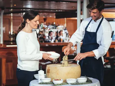 Ein Koch richtet an Bord der Sea Cloud Spirit frische Pasta aus einem großen Parmesanlaib für eine Gästin an.