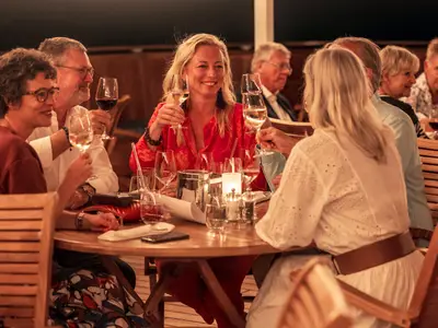 Eine heitere Gruppe von Gästen genießt Drinks und Wein an einem Holztisch auf dem Deck der Sea Cloud Spirit.