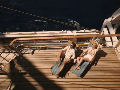 Vogelperspektive auf ein Paar, das auf blauen Liegestühlen auf dem Holdeck der Sea Cloud Spirit in der Sonne entspannt.