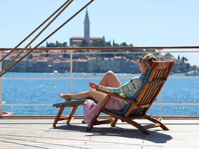 Eine Frau entspannt auf einer Holzliege an Bord der Sea Cloud Spirit und genießt die Aussicht auf die Küste.
