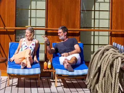 Ein Paar entspannt auf blauen Sonnenliegen an Bord der Sea Cloud Spirit und genießt Cocktails an Deck.
