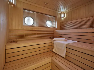 Blick in eine elegante Holzsauna mit gestuften Sitzbänken, Handtuch und Bullaugen an Bord der Sea Cloud Spirit.