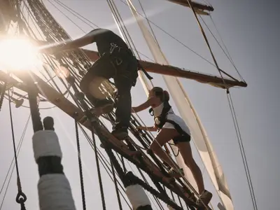 Zwei gesicherte Personen klettern im Gegenlicht der Sonne in den Wanten an Bord der Sea Cloud Spirit empor.