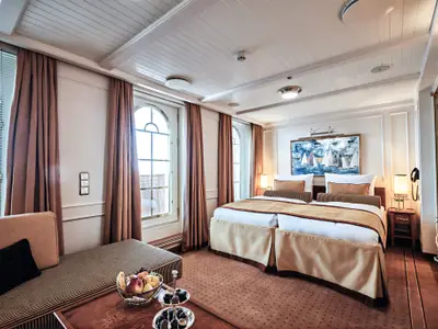 Luxuriös eingerichtete Suite an Bord der Sea Cloud Spirit mit großem Doppelbett, Sitzecke, Obstschale und Balkontür.