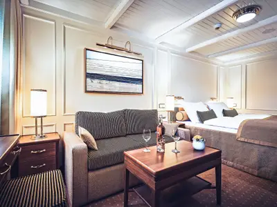 Elegante Suite an Bord der Sea Cloud Spirit mit gestreiftem Sofa, Holztisch mit Weingläsern und Doppelbett.