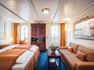 Luxuriös eingerichtete Suite an Bord der Sea Cloud Spirit mit Doppelbett, gestreiftem Sofa, Couchtisch und großen Bogenfenstern.