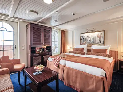 Schlafbereich einer luxuriösen Suite an Bord der Sea Cloud Spirit mit Doppelbett, Sitzgruppe und dunklen Holzmöbeln.