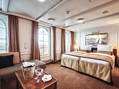Luxuriös gestaltete Suite an Bord der Sea Cloud Spirit mit Doppelbett, Holzelementen und Sektkühler im Vordergrund.
