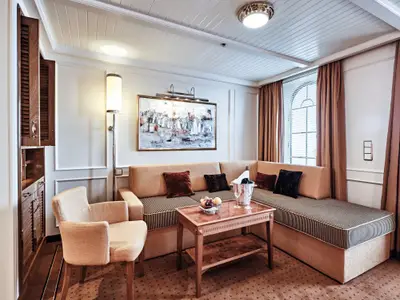 Wohnbereich einer Suite an Bord der Sea Cloud Spirit mit bequemem Ecksofa, Sessel, Couchtisch und Wandgemälde.
