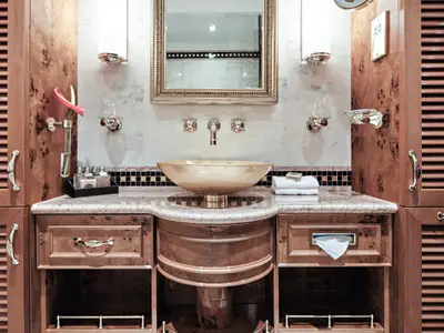 Ein edles Badezimmer an Bord der Sea Cloud Spirit mit einem vergoldeten Waschbecken, Holzschränken und Marmorwand.