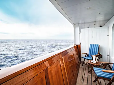 Veranda einer Suite an Bord der Sea Cloud Spirit mit blau gestreiften Holzstühlen und freiem Blick auf das Meer.
