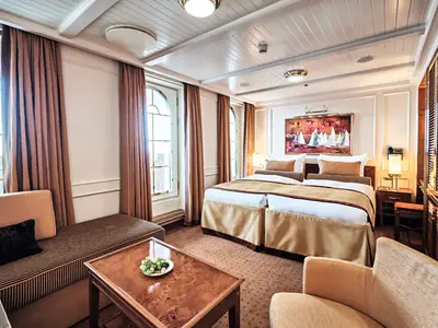 Geräumige Suite an Bord der Sea Cloud Spirit mit großem Bett, gemütlichem Sitzbereich und edlem Holzinterieur.