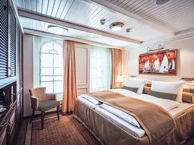 Blick in eine luxuriöse Suite an Bord der Sea Cloud Spirit mit großem Doppelbett, Sessel und Gemälde.