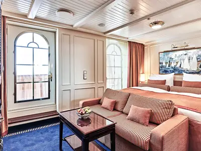 Elegante Junior Veranda Suite an Bord der Sea Cloud Spirit mit gestreiftem Sofa, großem Bett und Balkontür.