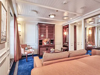 Blick in eine geräumige Junior Veranda Suite an Bord der Sea Cloud Spirit mit großem Bett, Holzschrank, Spiegel und Sesseln.