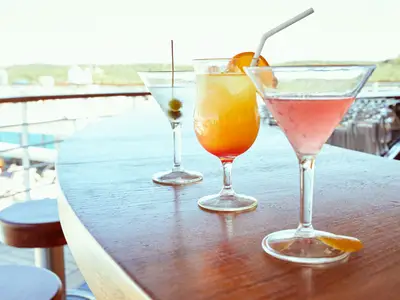 Drei bunte Cocktails auf einem Holztresen der Sky Bar an Bord der Seabourn Encore unter freiem Himmel bei Tageslicht.