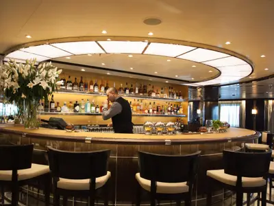 Ein Barkeeper bereitet Getränke an der eleganten, geschwungenen Bar an Bord der Seabourn Encore zu.