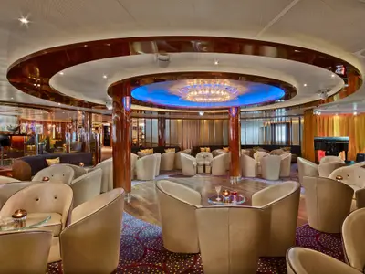 Blick in die luxuriöse Lounge „The Club“ an Bord der Seabourn Encore mit gemütlichen Sesseln, polierten Säulen und blauer Deckenbeleuchtung.