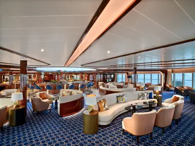 Elegante Lounge an Bord der Seabourn Encore mit geschwungenen Sofas, Sesseln, einer Bar im Hintergrund und Meerblick.