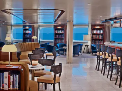 Die elegante Lounge Seabourn Square an Bord der Seabourn Encore mit gemütlichen Sesseln, Bücherregalen und Fenstern mit Blick auf das Meer.