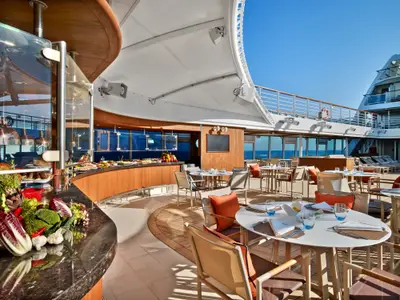 Eingedeckte Tische und ein Buffet-Tresen im Außenbereich des Restaurants an Bord der Seabourn Encore bei sonnigem Wetter.