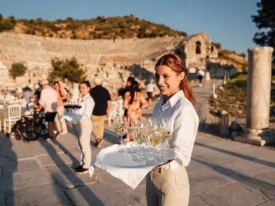 Eine lächelnde Kellnerin serviert Weißwein bei einer exklusiven Abendveranstaltung in Ephesus für Gäste der Seabourn Encore.