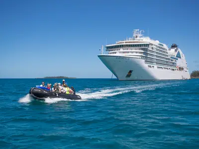 Ein vollbesetztes Zodiac-Schlauchboot fährt bei sonnigem Wetter auf dem blauen Meer vor der Seabourn Encore.