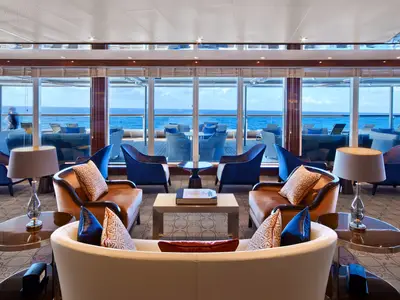 Elegante Lounge Seabourn Square an Bord der Seabourn Encore mit gemütlichen Sesseln, Lampen und großen Fenstern zum Meer.