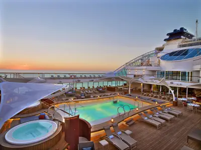 Blick auf das stimmungsvoll beleuchtete Pooldeck an Bord der Seabourn Encore mit Pool, Whirlpools und Liegestühlen während eines Sonnenuntergangs.