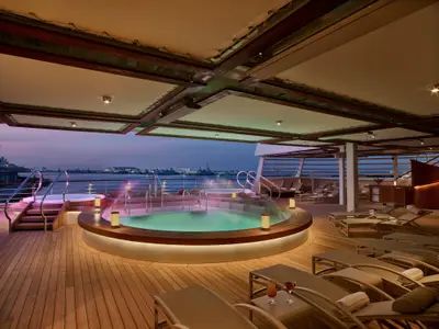 Der beleuchtete Whirlpool-Bereich auf dem Außendeck der Seabourn Encore in der Abenddämmerung mit Liegestühlen.