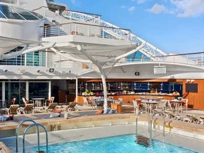 Das sonnige Pooldeck an Bord der Seabourn Encore mit Pool im Vordergrund, Tischen, Liegen und Buffetbereich unter Segeldächern.