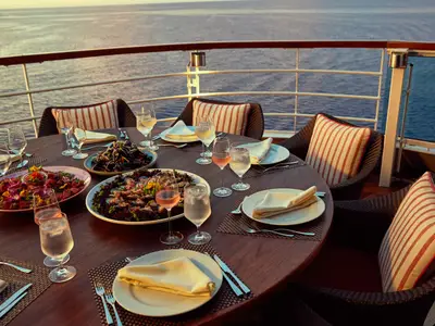 Ein elegant gedeckter Tisch mit Meeresfrüchten und Wein an Bord der Seabourn Encore bei Sonnenuntergang auf dem Meer.