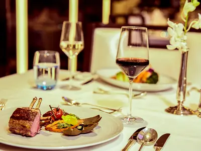 Ein elegant gedeckter Tisch an Bord der Seabourn Encore mit feinen Speisen wie Lammkarree, Rotwein und edlen Gläsern.