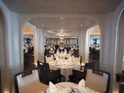 Einblick in das stilvolle Restaurant an Bord der Seabourn Encore mit weiß eingedeckten Tischen und geschwungenen Säulenbögen.