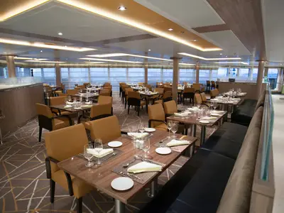 Blick in das elegant gestaltete Restaurant an Bord der Seabourn Encore mit gedeckten Tischen und Sesseln.