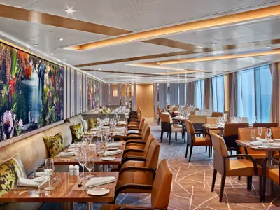 Das stilvoll eingerichtete Restaurant The Colonnade an Bord der Seabourn Encore mit eingedeckten Tischen und großen Panoramafenstern zum Meer.