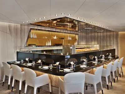 Modernes Sushi-Restaurant an Bord der Seabourn Encore mit einer eleganten schwarzen Theke und weißen Designer-Sesseln.