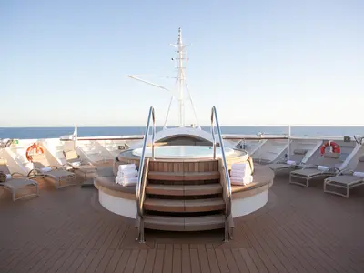 Ein hölzerner Whirlpool umgeben von Liegestühlen auf dem Sonnendeck der Seabourn Encore mit Blick auf das Meer.