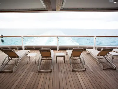 Einladende Liegestühle auf dem Holzdeck der Seabourn Encore mit freiem Blick auf das weite Meer und die Heckwelle.