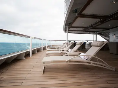 Reihe von eleganten Liegestühlen mit Handtüchern auf dem hölzernen Sonnendeck an Bord der Seabourn Encore bei freiem Blick auf das Meer.