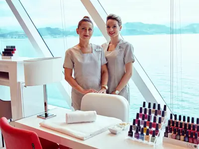 Zwei lächelnde Crew-Mitglieder des Spa-Bereichs an Bord der Seabourn Encore vor einem Nageltisch mit Blick auf das Meer.