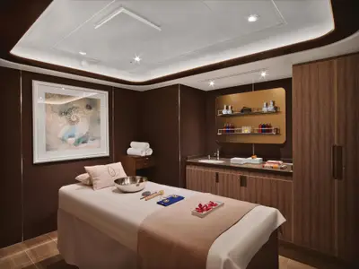 Ein elegant gestalteter Massageraum im Spa-Bereich an Bord der Seabourn Encore mit einer Massageliege und Holzelementen.