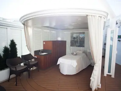 Ein luxuriöser Spa-Pavillon im Freien an Bord der Seabourn Encore, ausgestattet mit einer Massageliege, Sesseln und fließenden Vorhängen.